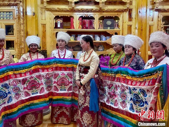 圖為女性展示村民自發(fā)繡制的“百米五彩哈達(dá)”?！±钣穹?攝